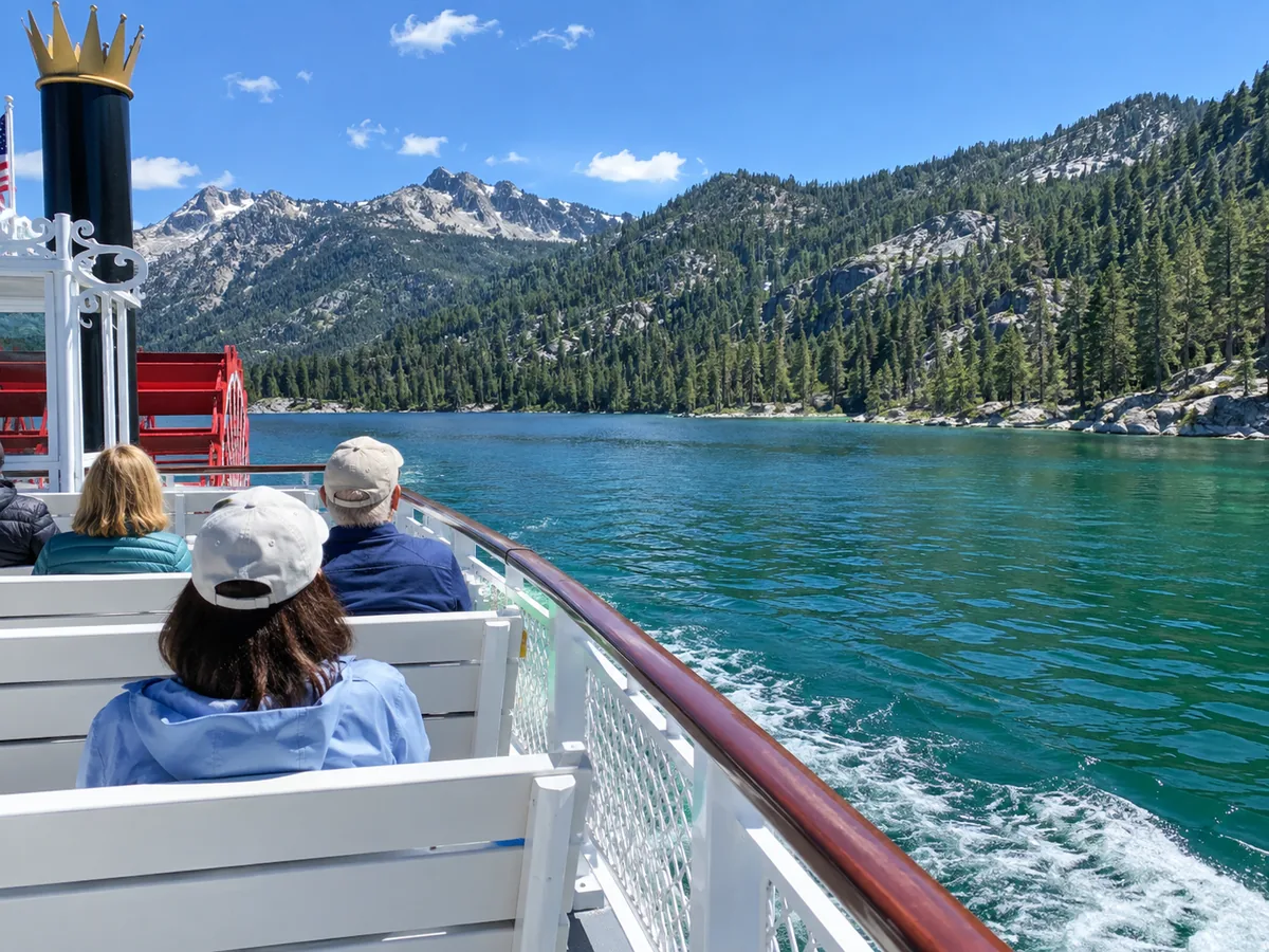 Passagers vus de dos sur le pont supérieur ouvert d'un bateau à roue à aubes, contemplant l'eau émeraude et les montagnes boisées
